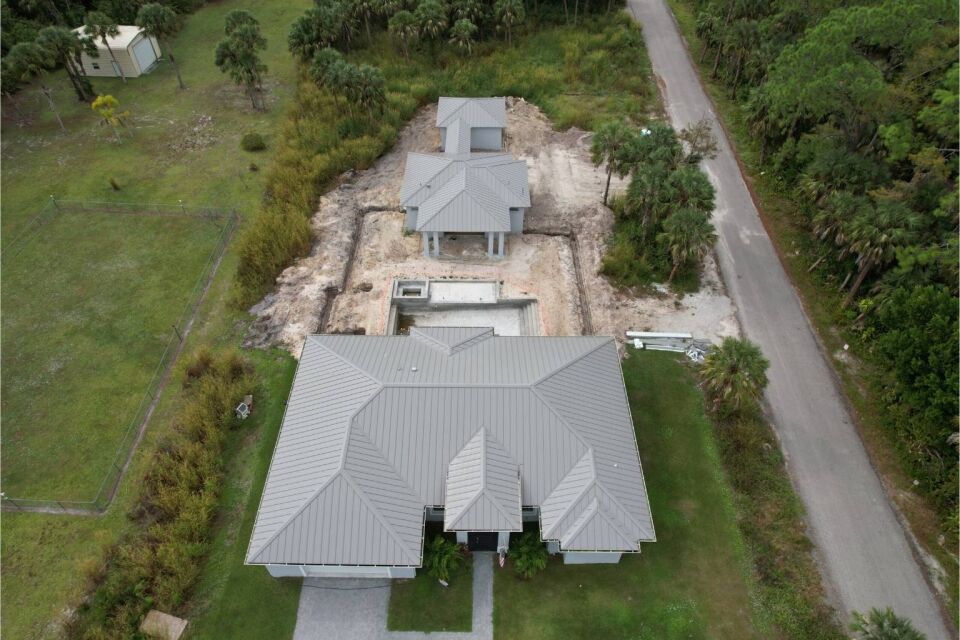 Aerial view of a new construction metal roof installation on a modern residential home and matching detached garage.