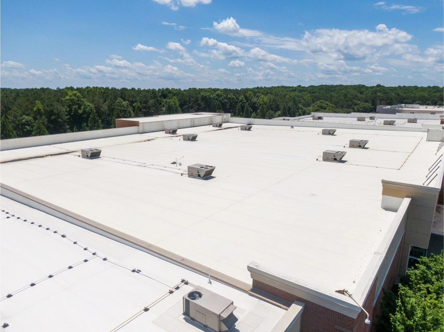 Wide aerial view of a newly installed commercial TPO flat roof replacement featuring roof-mounted AC units in Collier County.