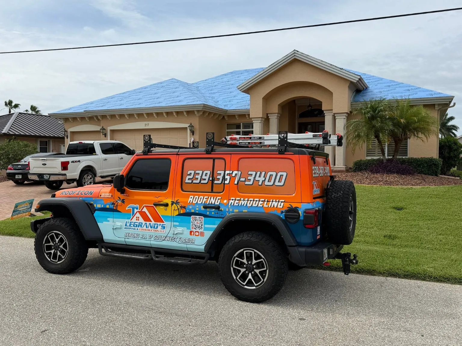 Legrand's Roofing branded Jeep service vehicle with a ladder rack parked in front of a home with a blue weather barrier during the 217 project.