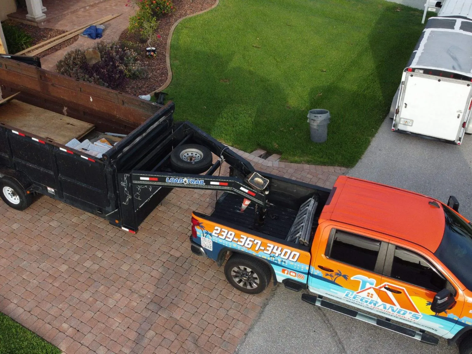 Aerial perspective of a Legrand's Roofing branded service truck parked with a large Load Trail dump trailer during the 217 re-roof project.