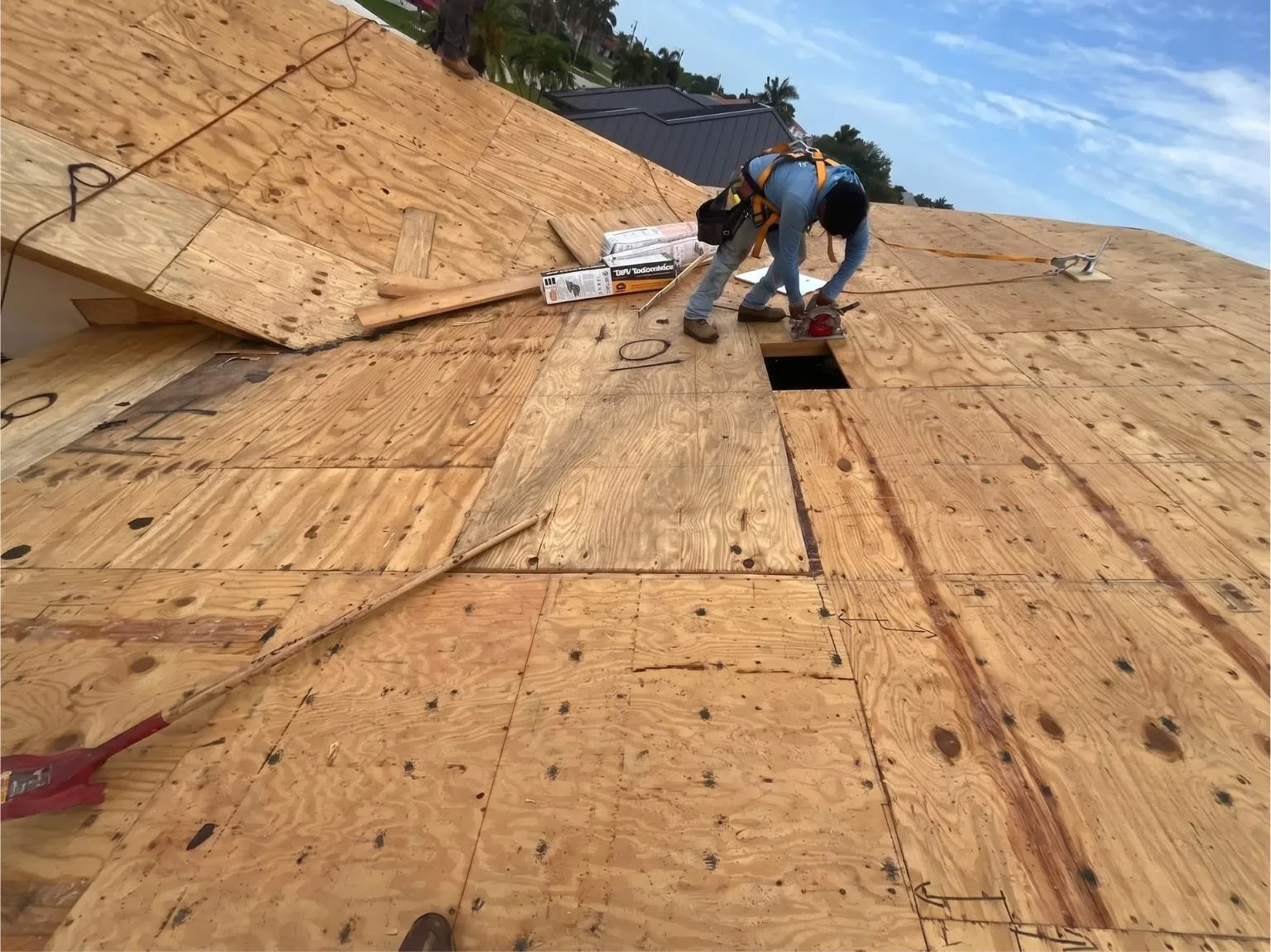A technician from Legrand's Roofing uses a circular saw to trim wood sheathing during the 217 re-roof installation phase.