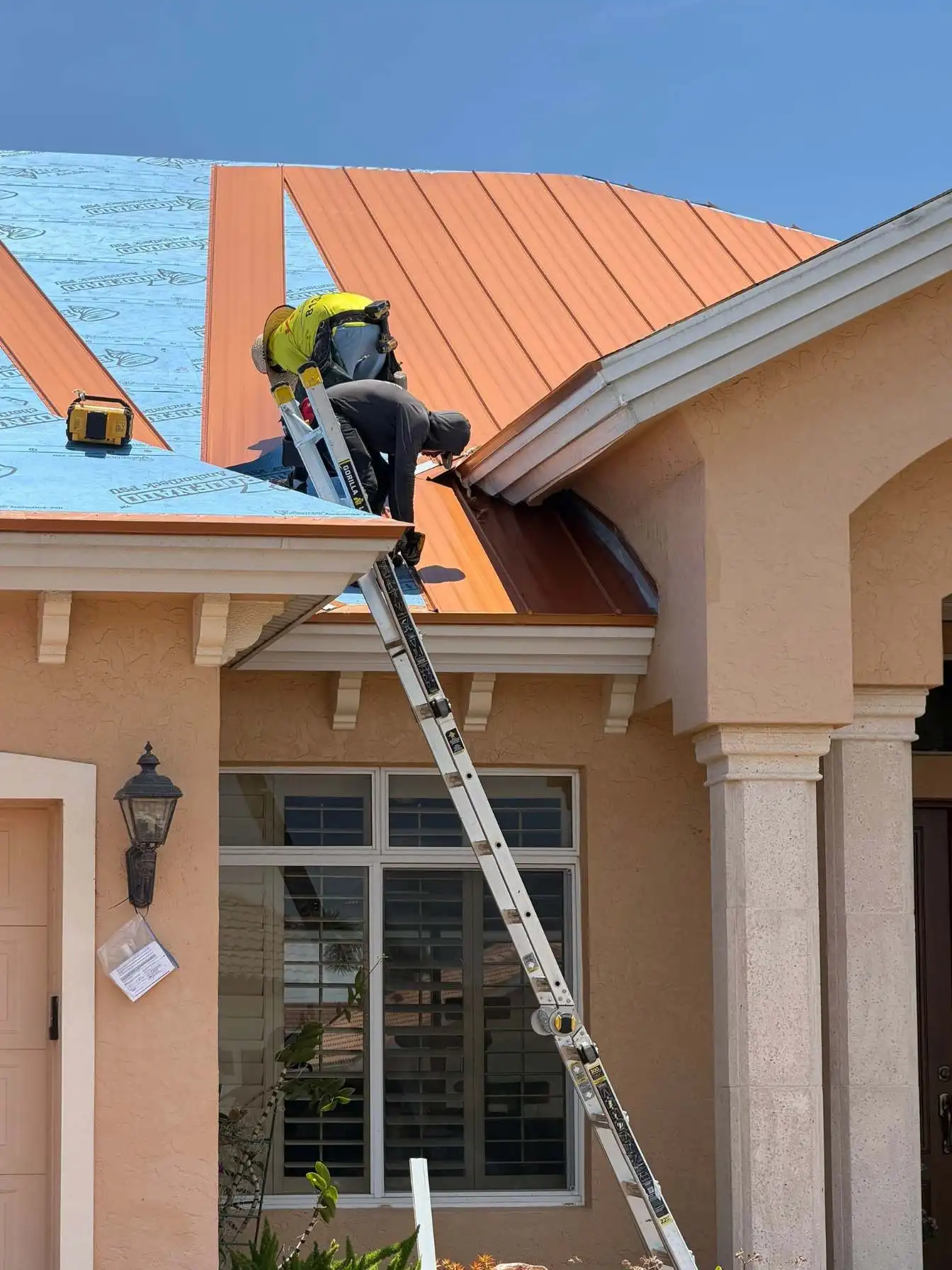 LeGrand's Roofing technicians installing premium copper-colored standing seam metal roof panels over blue AnchorLock underlayment.