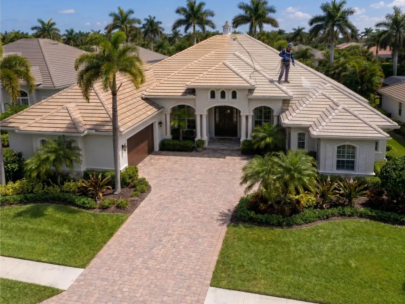 A professional worker wearing a safety harness performs low-pressure soft wash roof cleaning on a clean, luxury tile-roof single-family home in Naples, Florida