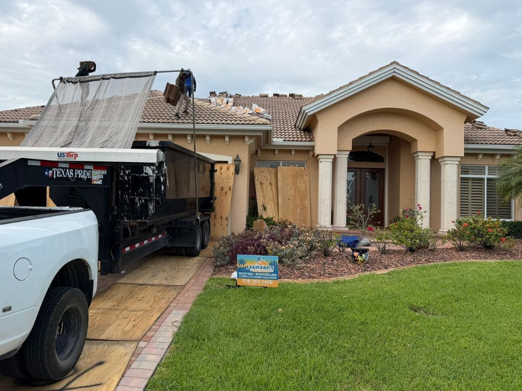 Residential tile roof repair in progress with roofing crew, dump truck, and Legrand’s Roofing sign outside a Florida home.