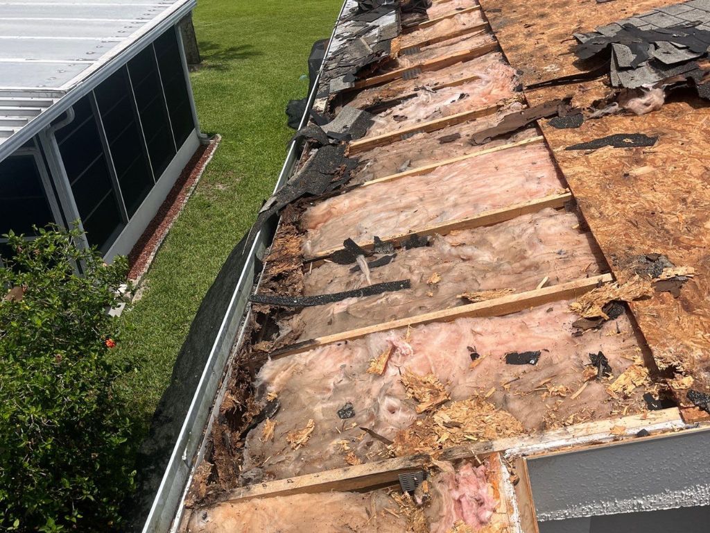 Exposed roof decking with water damage and torn shingles, showing the need for roof repair or replacement.