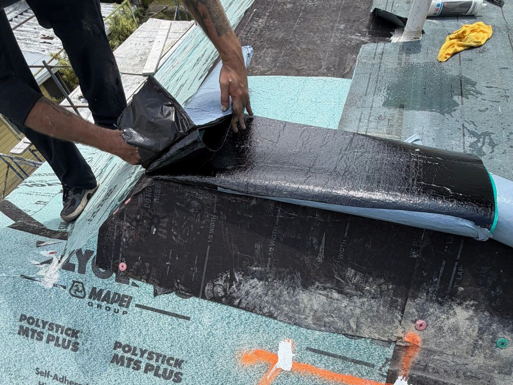 Roofer installing a waterproofing membrane on a roof to prevent leaks, water damage, and storm-related roofing issues.