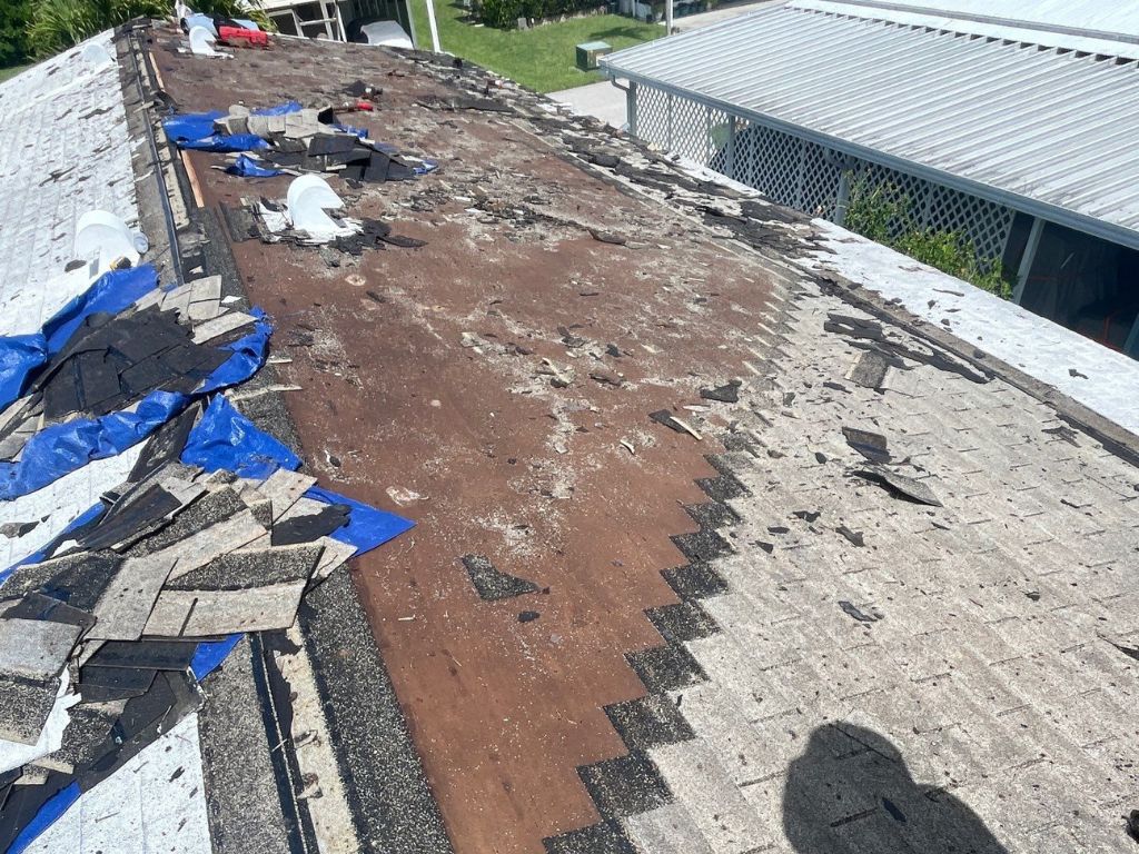 Storm-damaged shingle roof with missing shingles, exposed underlayment, and tarps showing need for emergency roof repair.