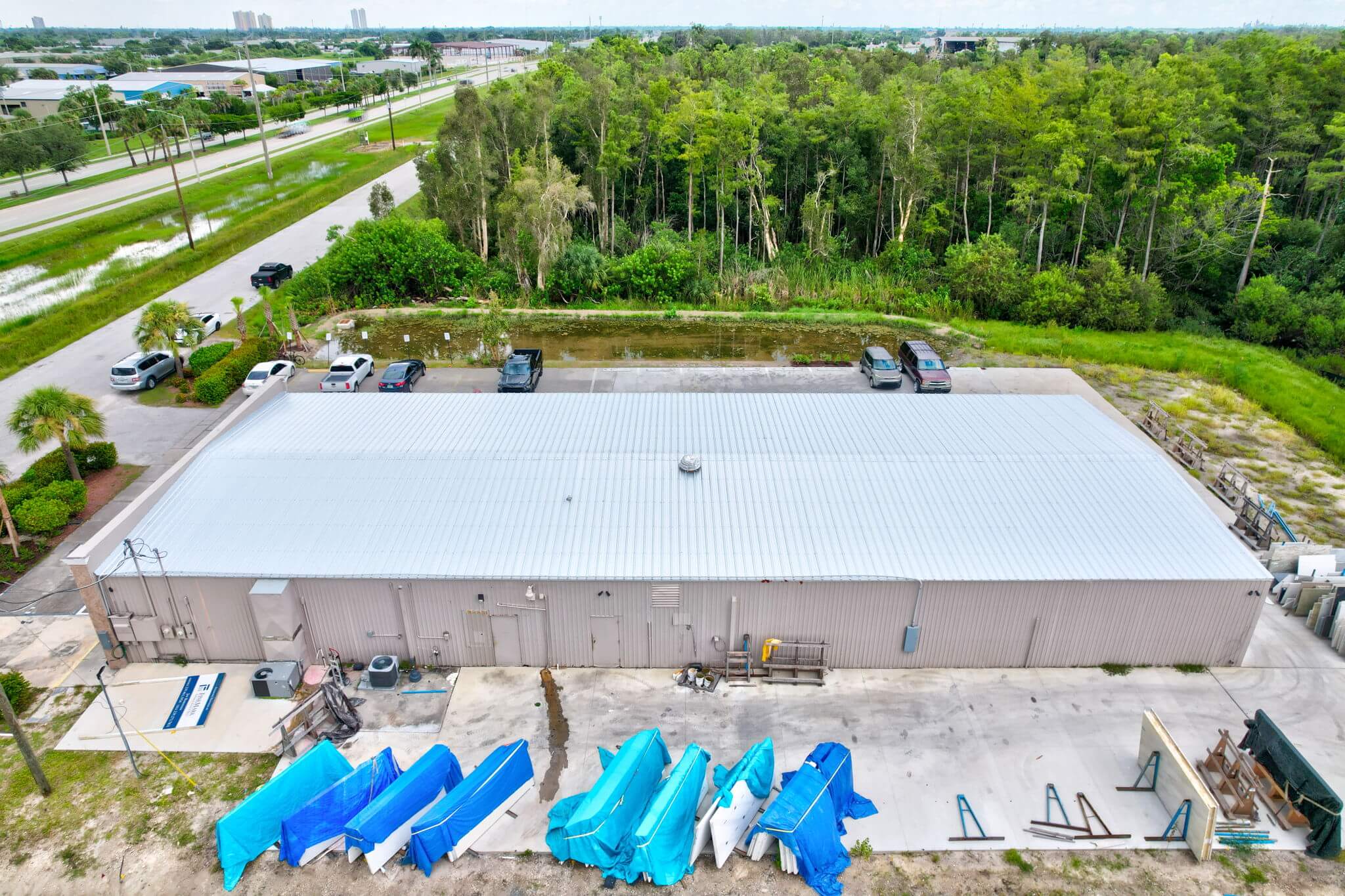 Side aerial drone view of commercial building metal roof facing forest backdrop.