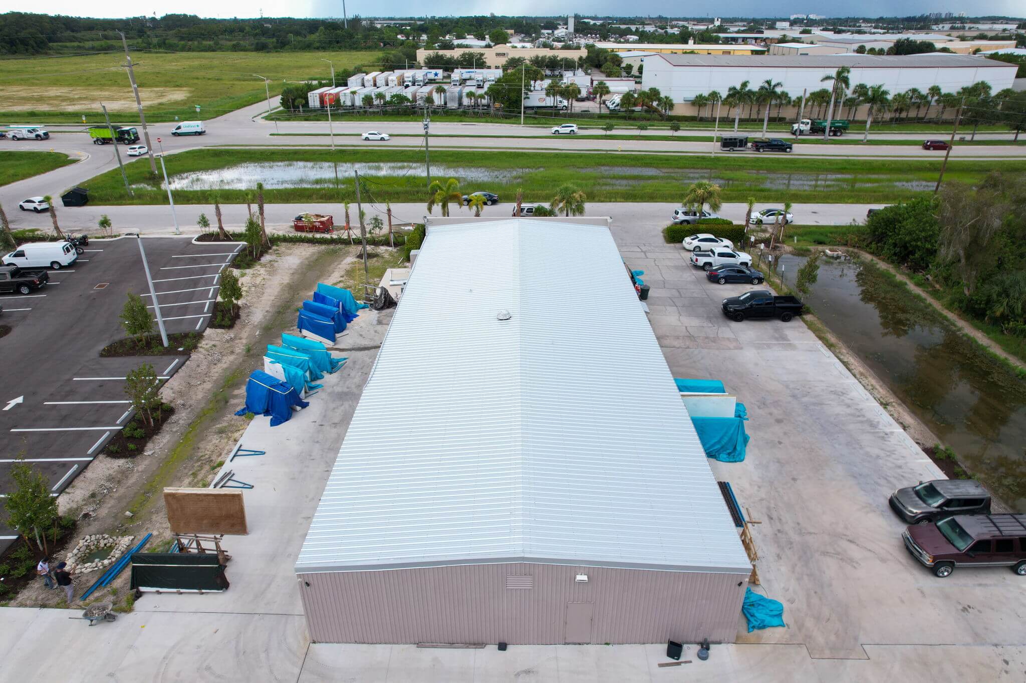 Rear elevated drone shot of commercial building's metal roof looking toward the main road.