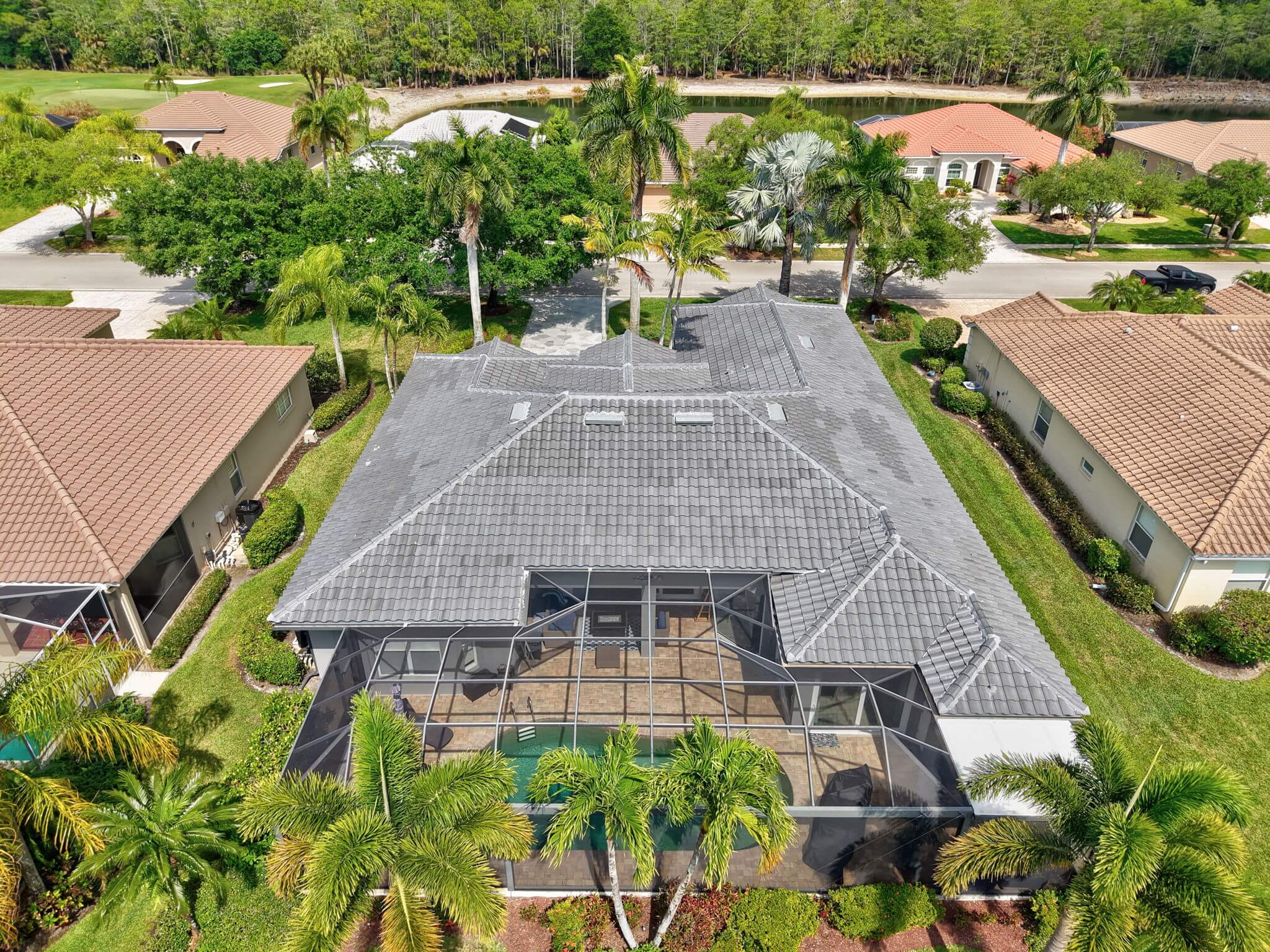 Rear aerial drone shot of grey tile roof over pool cage with golf course and lake backdrop.