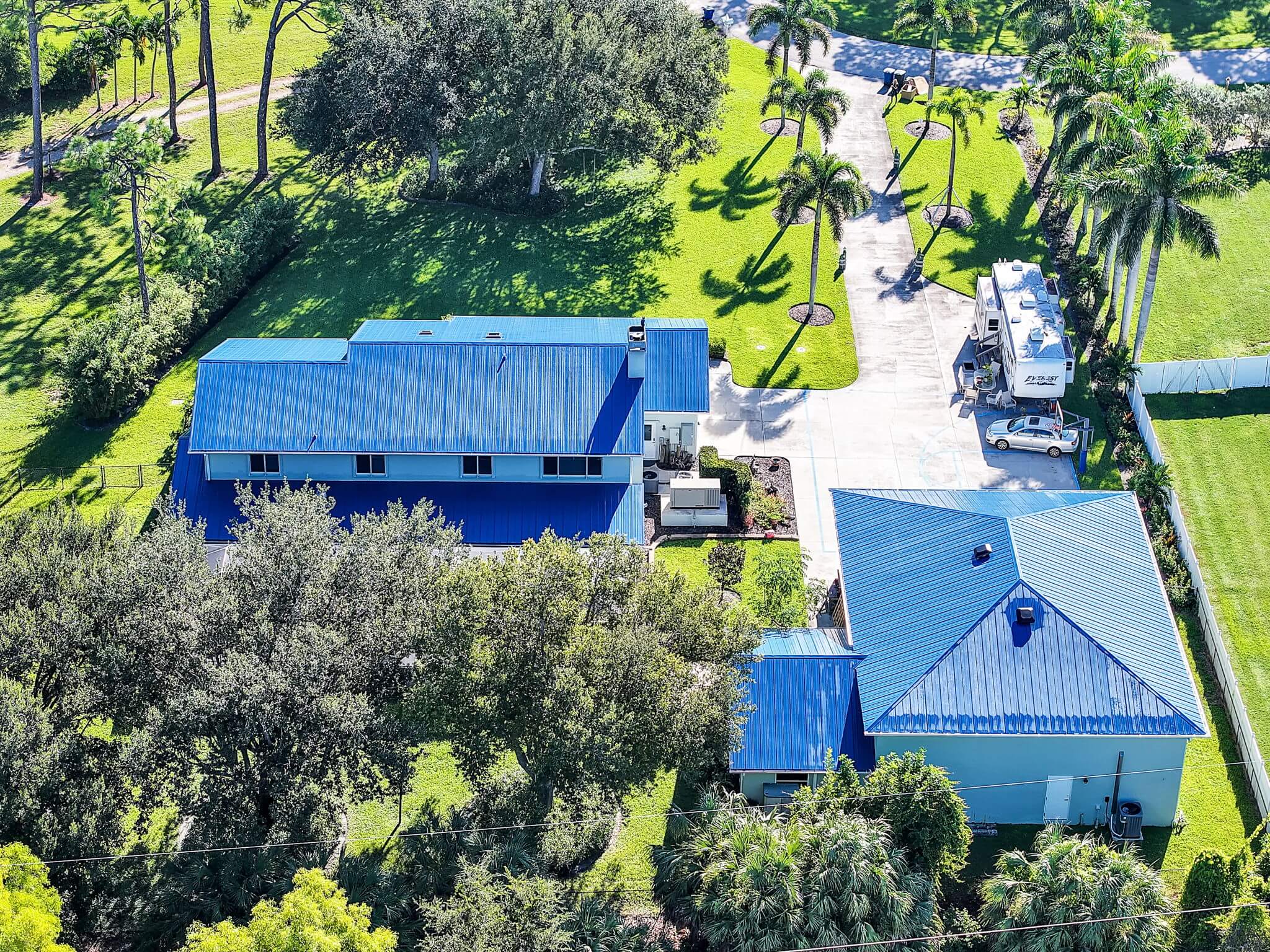 Elevated side aerial view showcasing both the main home and detached garage metal roofs surrounded by trees.