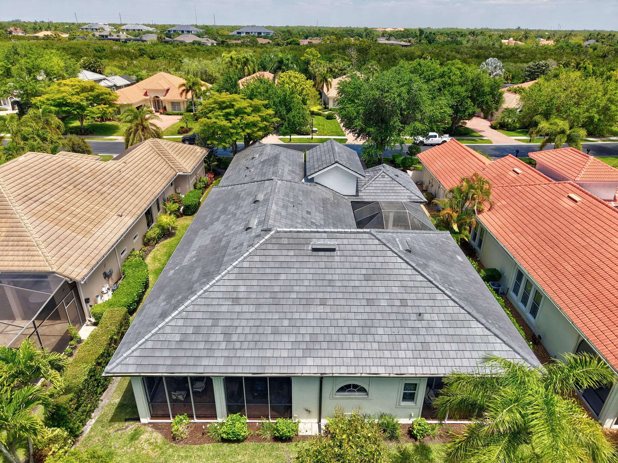 Rear high-angle drone shot looking down the roofline from above the screened patio area toward the street.