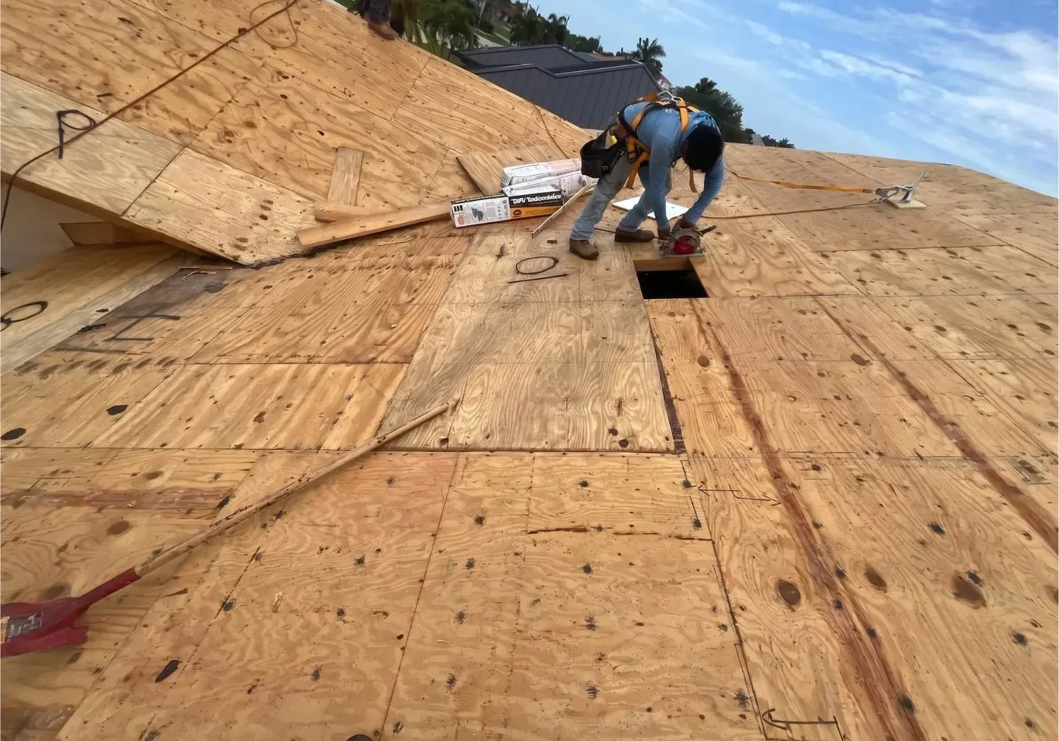 A technician from Legrand's Roofing uses a circular saw to trim wood sheathing during the 217 re-roof installation phase.