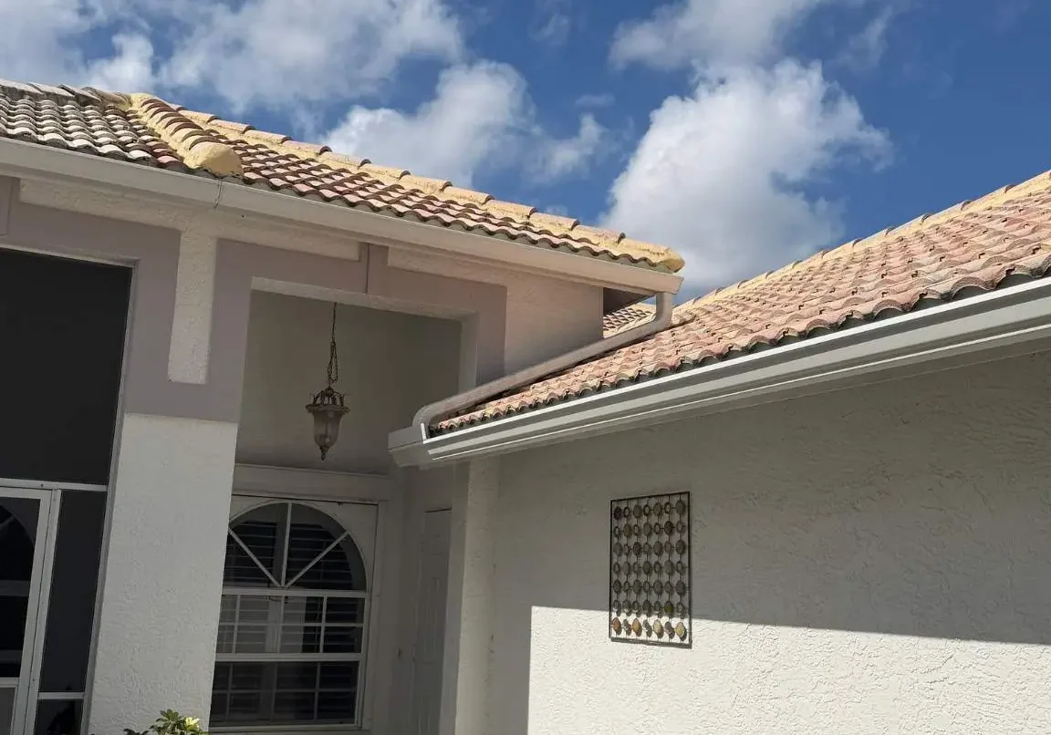 Detailed view of the home's front courtyard entryway showing seamless white gutter installations and concrete tile trim profiles.