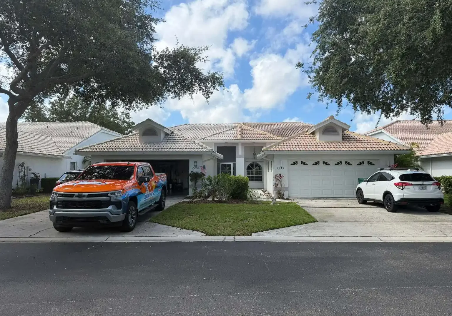 Wide front street view of adjacent stucco homes with concrete tile roofs, featuring a staged service vehicle in the driveway.