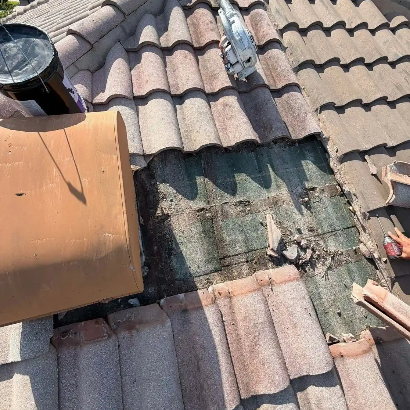 An active tile roof repair job site by LeGrand's Roofing showing a stripped-away section near an off-ridge vent, exposing the underlying green felt layer.