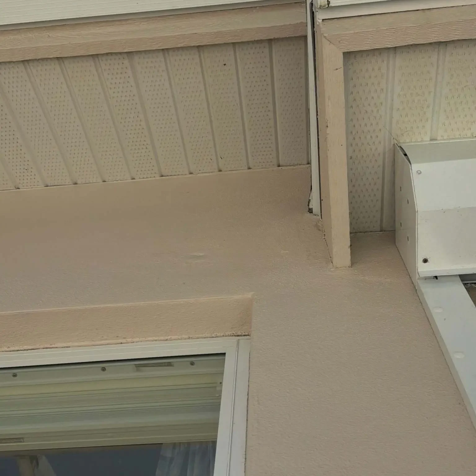 Close-up under-eave perspective of a corner junction where the aluminum fascia strip meets a textured soffit ceiling panel on June 12.