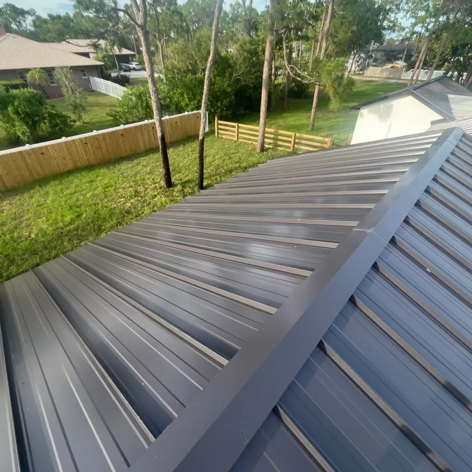 High-angle perspective of a freshly completed dark gray standing seam metal roof ridge and panels installed by Legrand's Roofing on June 12.