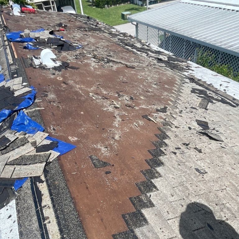 Storm-damaged shingle roof with missing shingles, exposed underlayment, and tarps showing need for emergency roof repair.