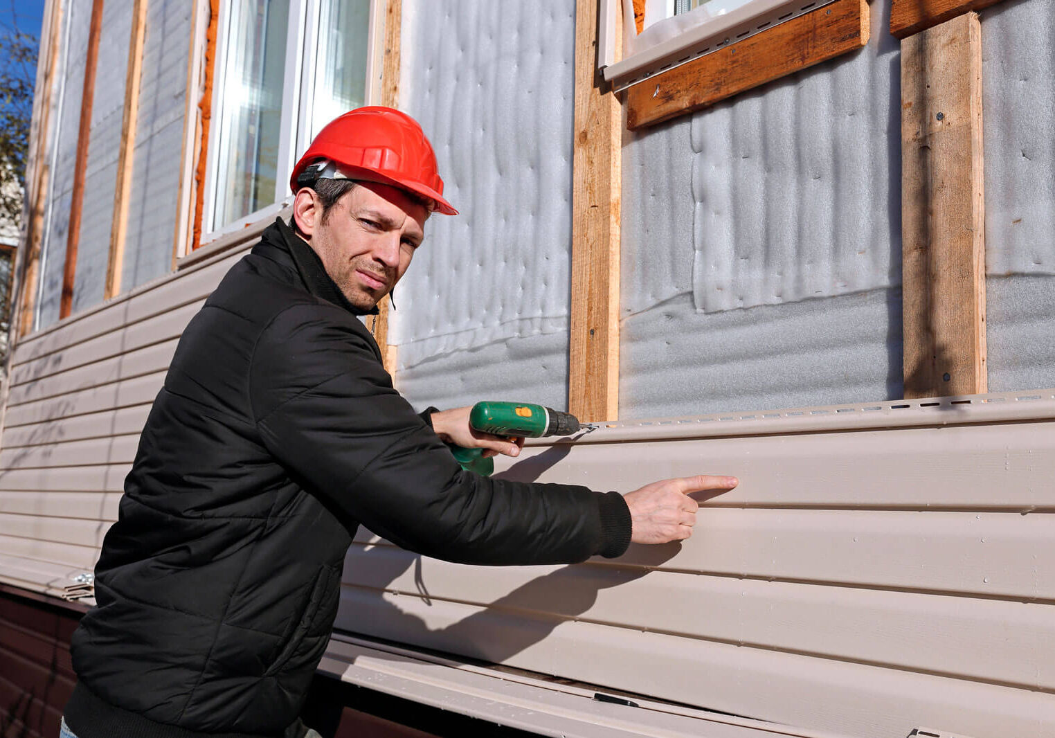 A worker installs panels beige siding on the facade